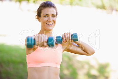 Fit woman exercising with dumbbells in the park