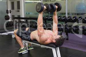 Shirtless bodybuilder lying on bench lifting heavy dumbbells