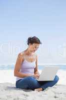 Pretty brunette using laptop on the beach