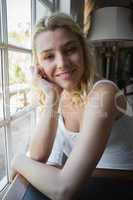 Pretty blonde sitting by the window smiling at camera