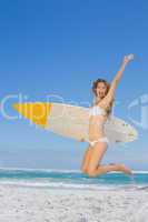 Smiling surfer girl holding her surfboard and jumping on the bea