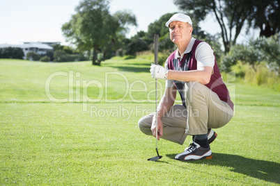 Confident golfer kneeling holding his golf club