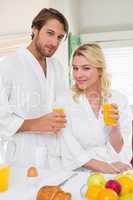 Cute couple in bathrobes smiling at camera together having break