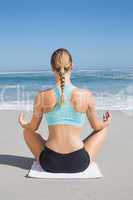 Fit woman sitting on the beach in lotus pose