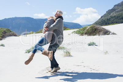 Smiling couple playing on the beach in warm clothing
