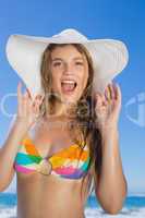 Beautiful girl in bikini and straw hat looking at camera on beac