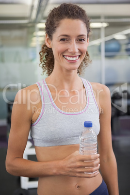 Fit woman smiling at camera holding water bottle