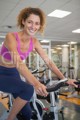 Pretty fit woman on the spin bike smiling at camera