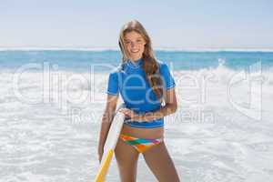 Fit smiling surfer girl on the beach with her surfboard