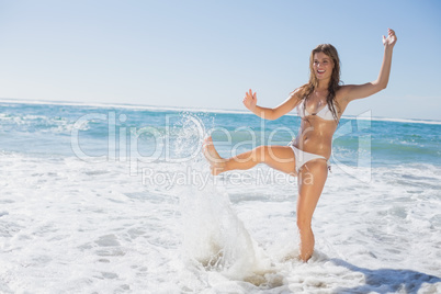 Beautiful smiling woman in white bikini splashing on the beach