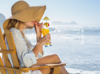 Smiling blonde relaxing in deck chair by the sea sipping cocktai