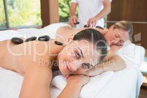 Pretty friends lying on massage tables with hot stones on their