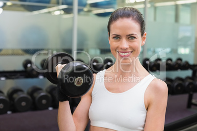 Fit smiling brunette lifting heavy black dumbbell