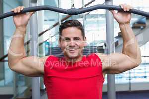 Handsome smiling bodybuilder using weight machine for arms