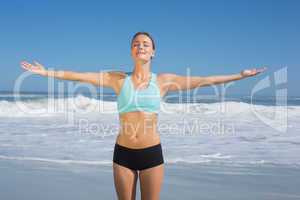 Fit woman standing on the beach with arms out