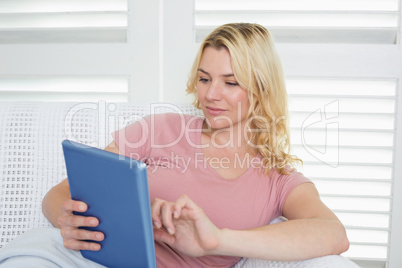 Happy blonde relaxing on the couch with her tablet pc