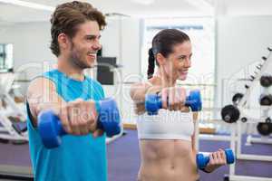 Fit couple exercising with blue dumbbells and smiling