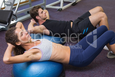 Fit man and woman doing sit ups on exercise ball