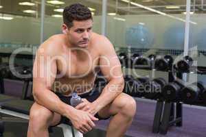Shirtless bodybuilder sitting on bench with water bottle