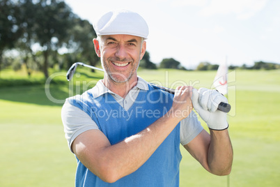 Golfer standing and swinging his club smiling at camera