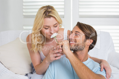Happy casual couple hugging on couch with man offering tiny flow