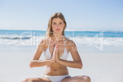 Beautiful girl in white bikini sitting in lotus pose on beach