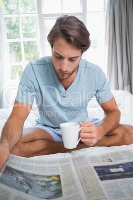 Handsome man sitting on bed reading the paper with coffee
