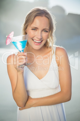 Smiling blonde standing at the beach in white sundress with blue