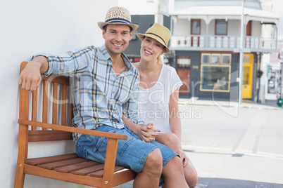 Young hip couple sitting on bench smiling at camera