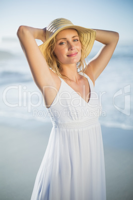 Smiling blonde standing at the beach in white sundress and sunha