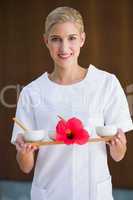 Smiling beauty therapist holding tray of treatments