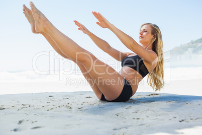 Fit blonde in core balance pilates pose on the beach