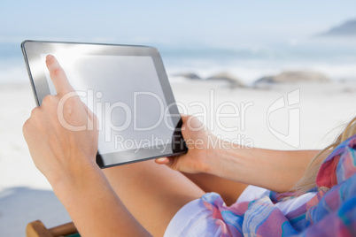 Woman sitting on beach in deck chair using tablet pc