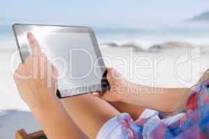 Woman sitting on beach in deck chair using tablet pc