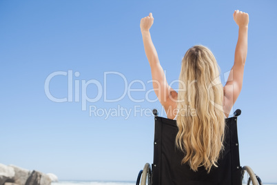 Wheelchair bound blonde sitting on the beach with arms up