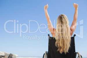 Wheelchair bound blonde sitting on the beach with arms up