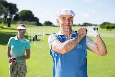 Happy golfer teeing off with partner behind him