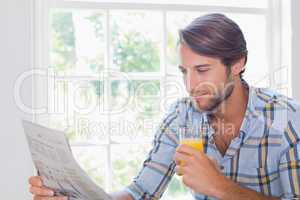 Casual smiling man having orange juice while reading newspaper