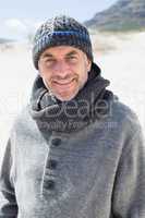 Attractive man smiling at camera on the beach in hat and scarf