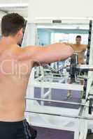 Shirtless focused bodybuilder lifting heavy barbell weight looki