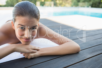 Smiling brunette lying on a towel poolside