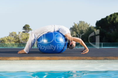 Peaceful brunette in cobra pose over exercise ball poolside