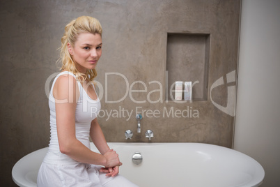 Pretty blonde sitting by the bath smiling at camera