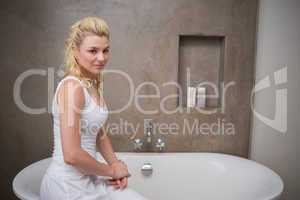 Pretty blonde sitting by the bath smiling at camera