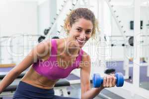 Pretty fit woman lifting blue dumbbell sitting on bench