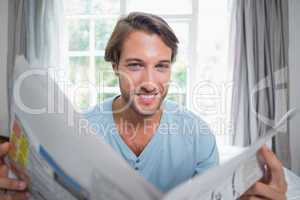 Handsome smiling man sitting on bed reading the newspaper