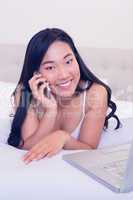 Asian waitress smiling at camera lying on bed talking on phone