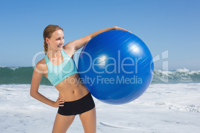 Fit woman standing on the beach holding exercise ball