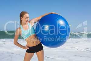 Fit woman standing on the beach holding exercise ball