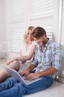 Young couple sitting on floor using laptop